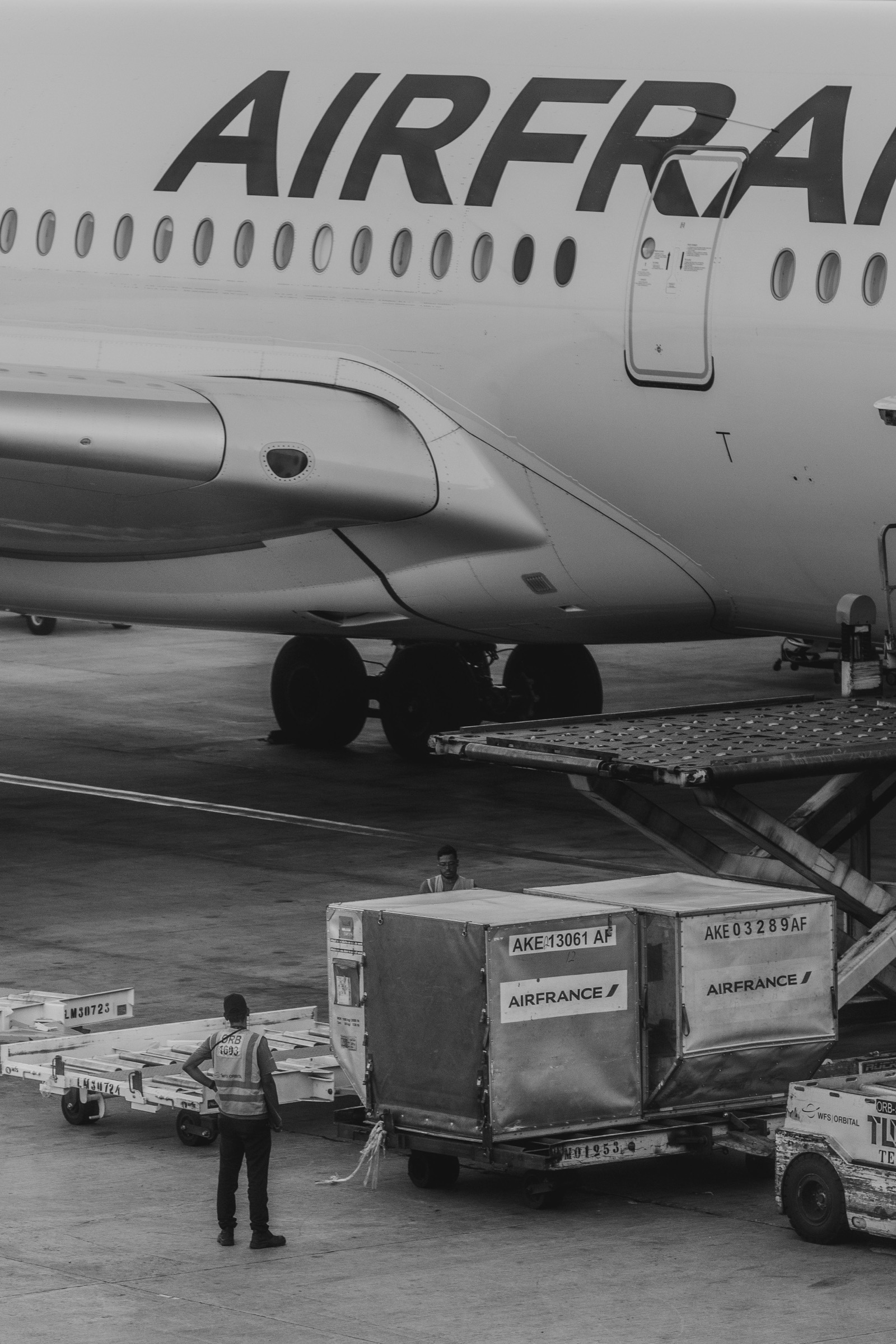 Contenedores ULD tipo AKE (LD3) sobre dollies, listos para cargarse a la bodega de un avión en plataforma